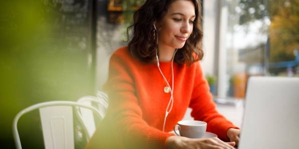 Frau arbeitet mobil von einem Café aus an ihrem Laptop.