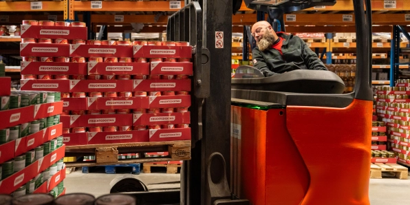 Skladník na červenom vysokozdvižnom vozíku naberá palety s konzervami