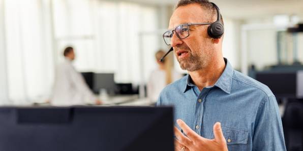Kaufland-Mitarbeiter mit Headset vor einem Bildschirm in angeregtem Gespräch bei einer Telko.