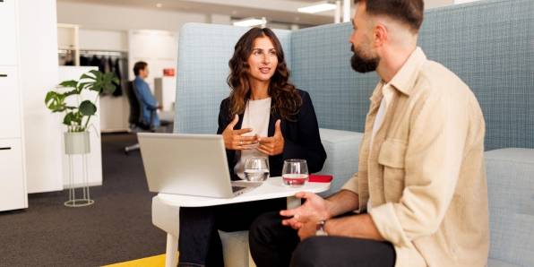 Mitarbeiterin und Mitarbeiter sitzen mit Laptop zu einer Besprechung in lockerer Atmosphäre auf einer stylischen Sitzbank.