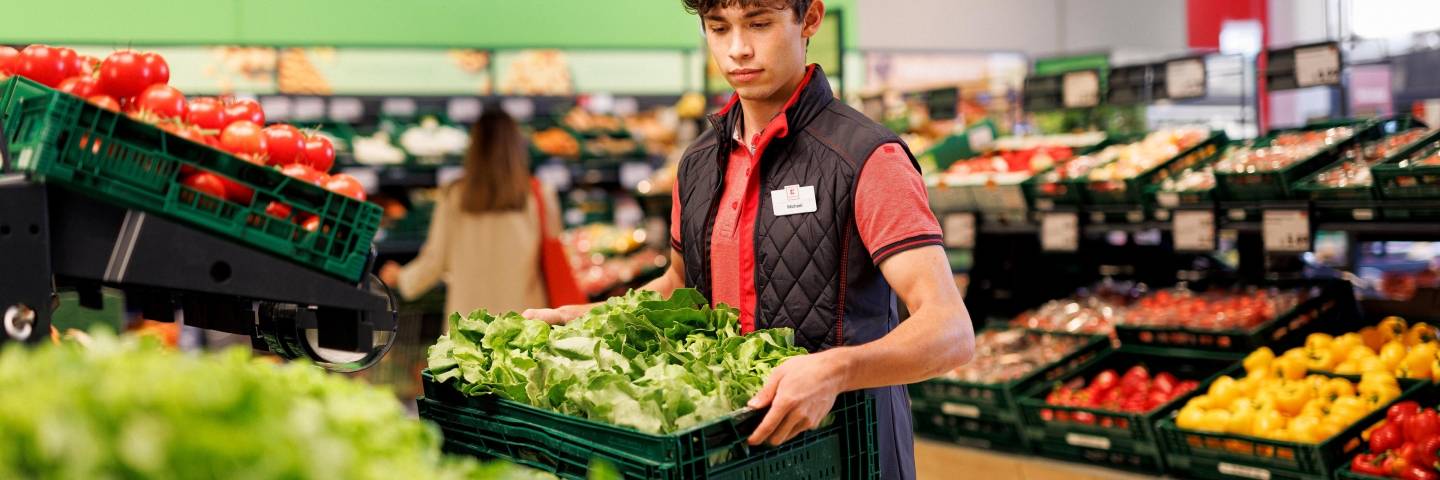 Obst- und Gemüsebereich einer Kaufland-Filiale: Junger Verkaufsmitarbeiter verräumt eine Box mit Salat.