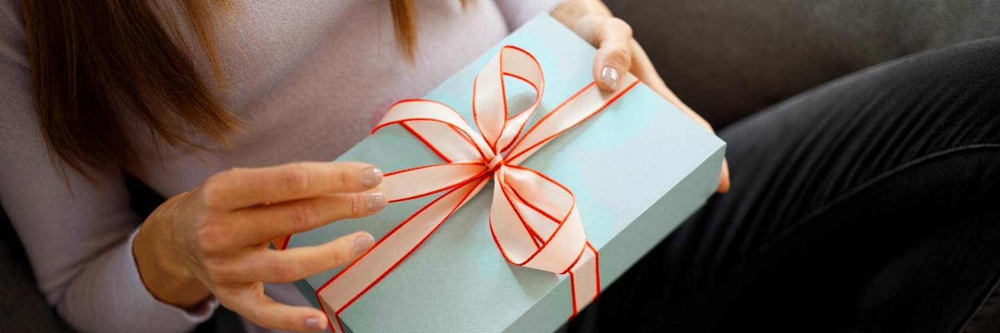 Frau sitzt auf einem Sofa und hält ein blau verpacktes Geschenk in der Hand.