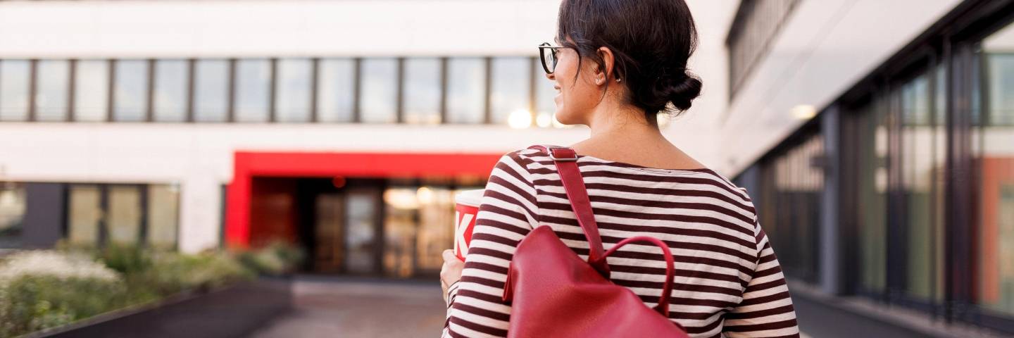 Mitarbeiterin mit rotem Rucksack auf dem Weg in ein Kaufland-Bürogebäude.