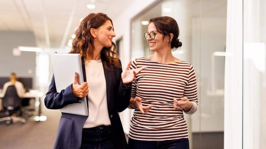 2 Kolleginnen auf dem Flur im Kaufland-Büro lachend im Gespräch.