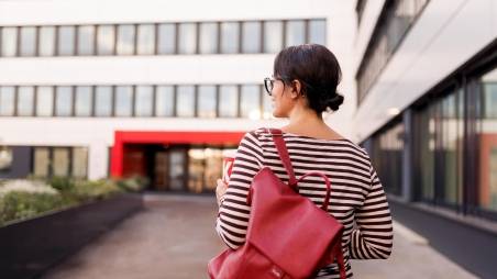 Mitarbeiterin mit rotem Rucksack auf dem Weg in ein Kaufland-Bürogebäude.