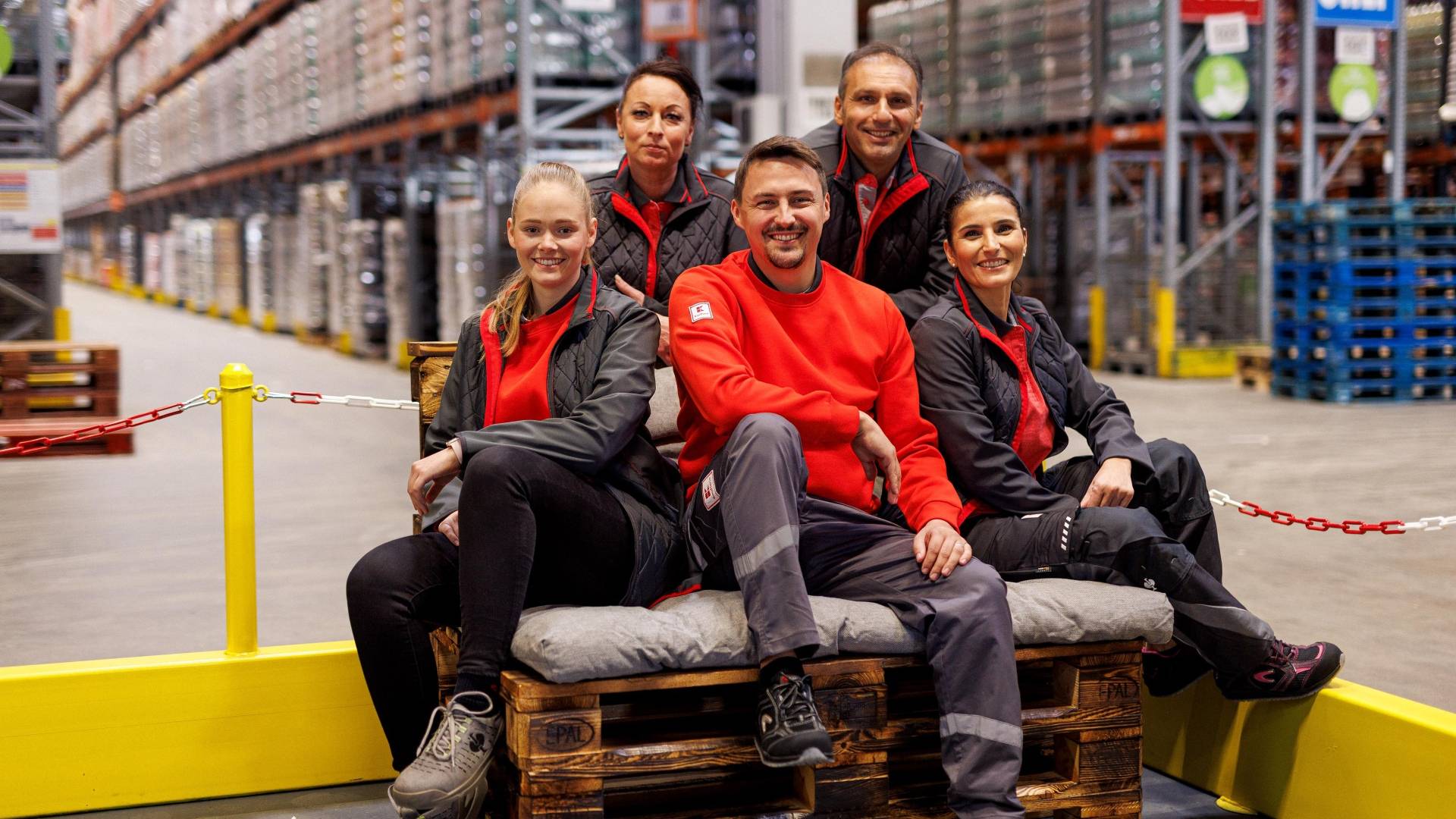 Fünf Logistikmitarbeiter von Kaufland haben zum Gruppenfoto auf einer Palette Platz genommen.
