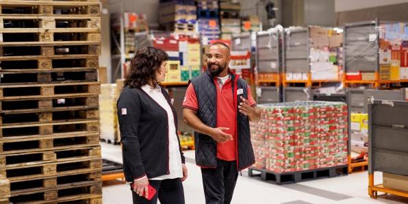 Im Filiallager: Kaufland-Verkaufsmitarbeiter im Gespräch mit einer Kollegin. Im Hintergrund ein Stapel Paletten.